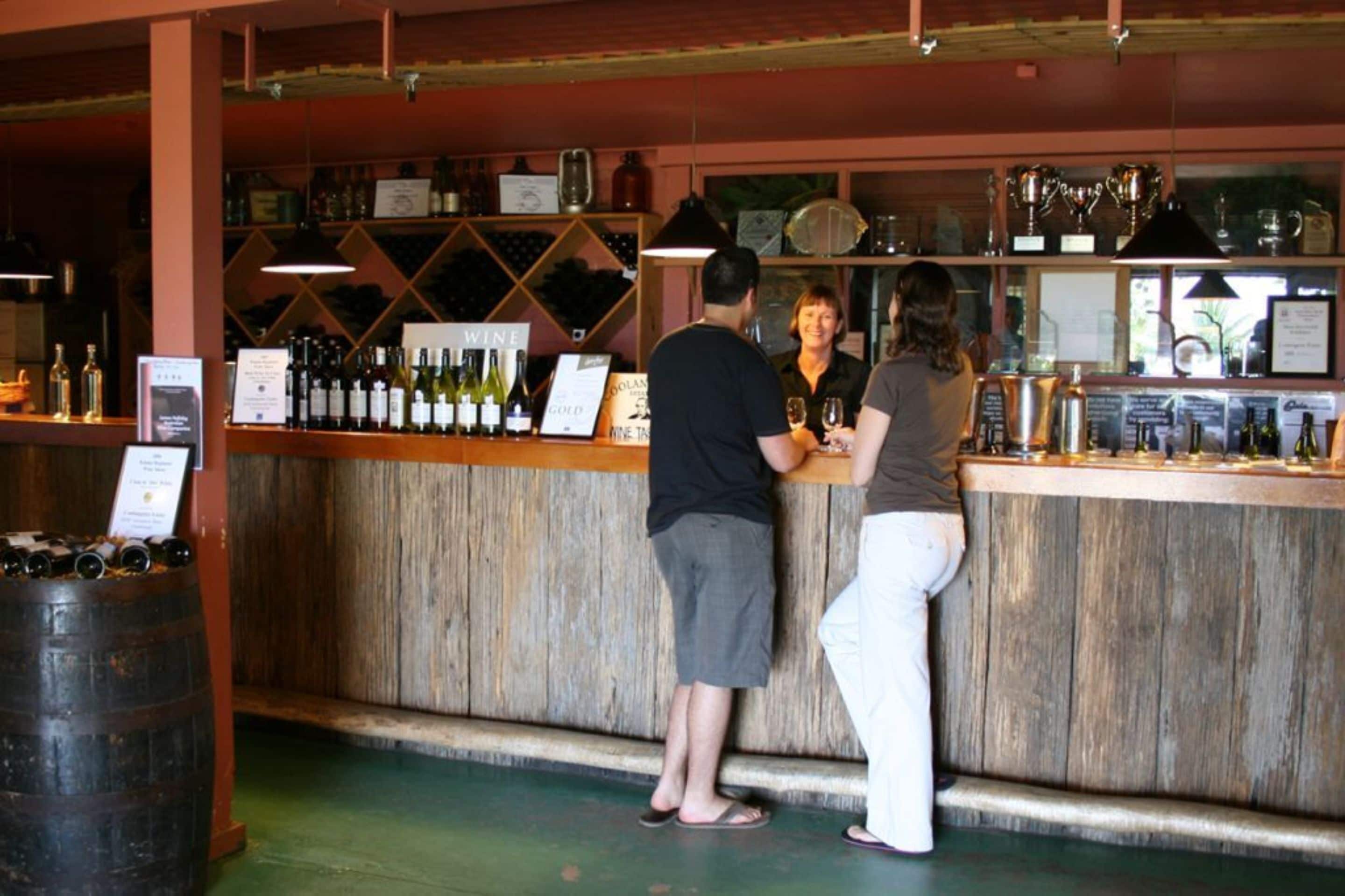 A bar with a wooden counter, shelves with bottles, and a sign indicating a wine list.