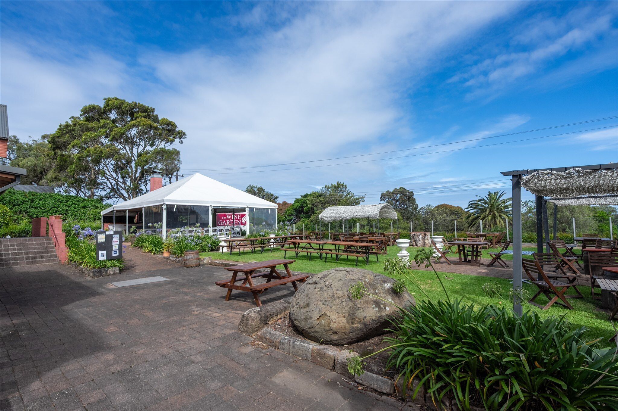 Un espacio de comedor al aire libre con mesas de picnic, una carpa blanca y un letrero que dice "The Wine Garden".