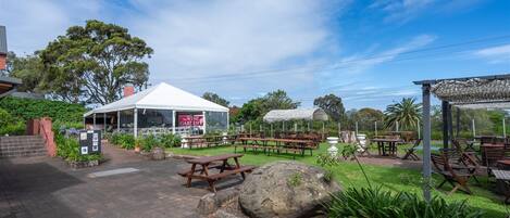 An outdoor dining area with picnic tables, a white tent, and a sign for "The Wine Garden."