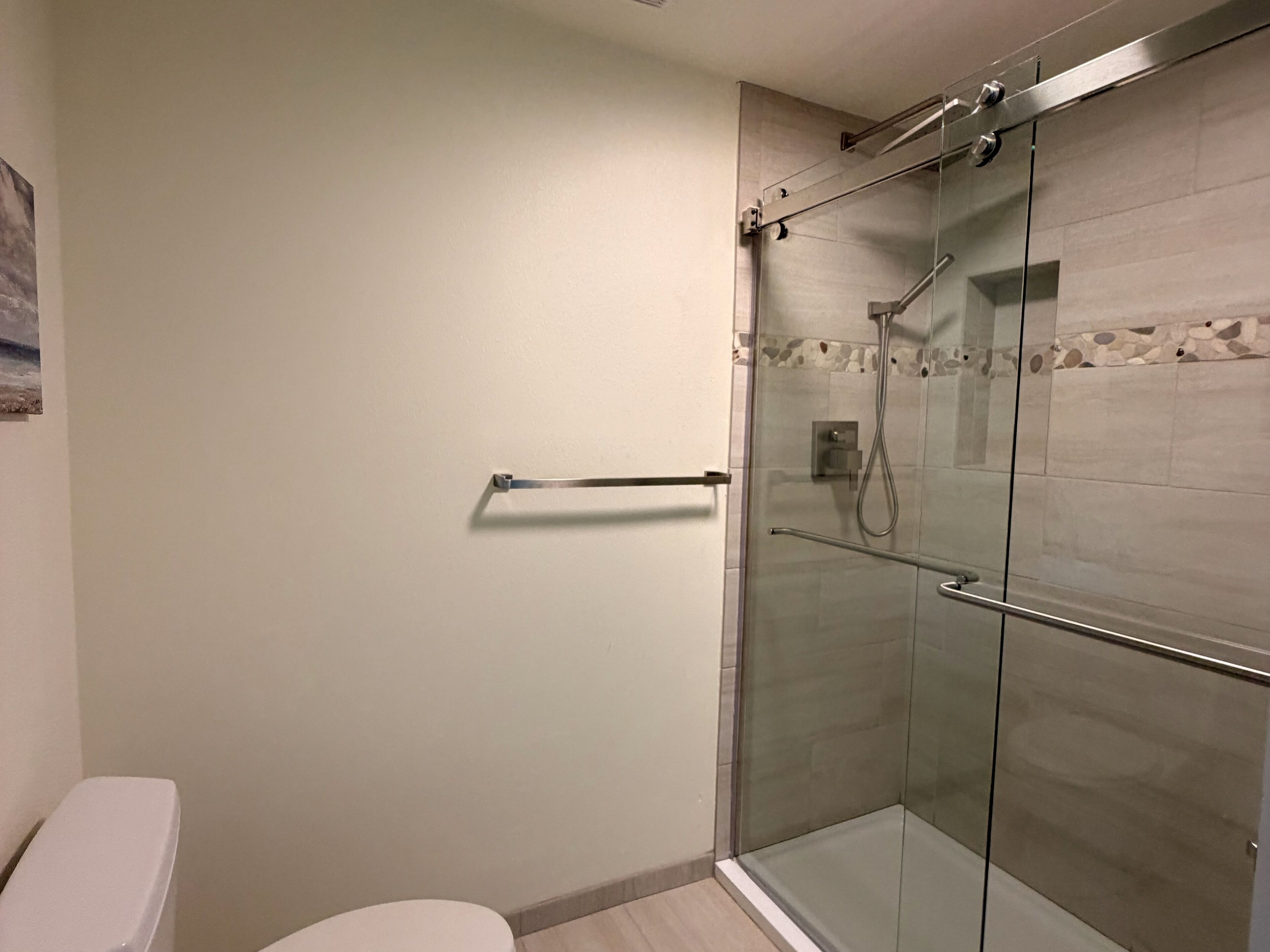 Een moderne badkamer met een glazen douchecabine, toilet en een handdoekhouder.
