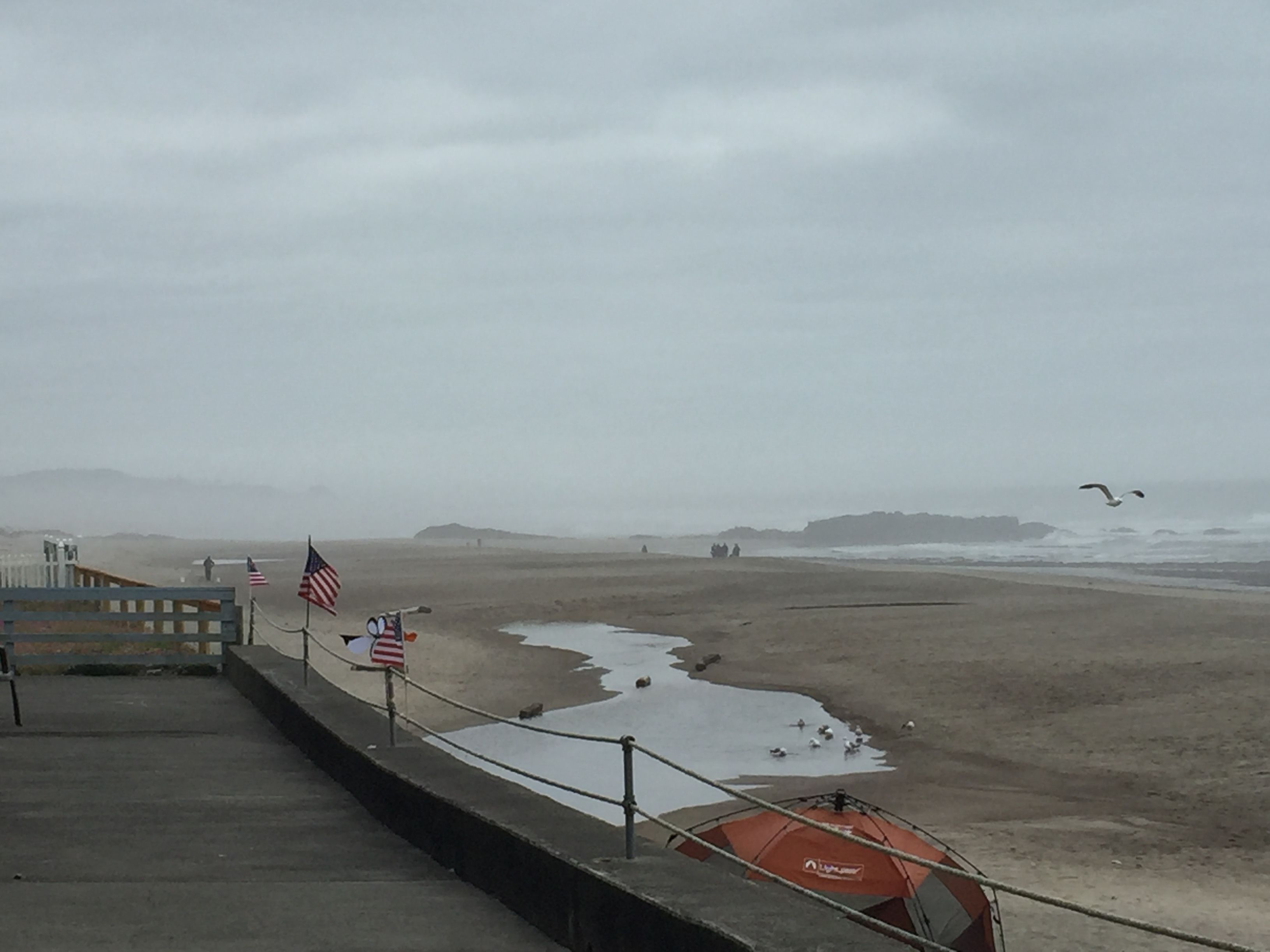 En strand med en støbt gangsti, amerikanske flag og en rød parasol.
