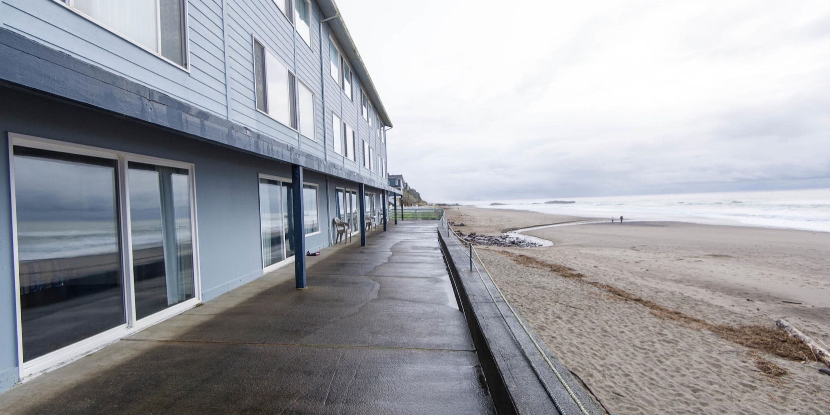 Ein Gebäude direkt am Strand mit großen Fenstern und einem betonierten Gehweg, der zum Strand führt.