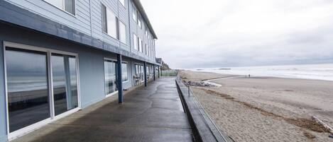 Ein Gebäude direkt am Strand mit großen Fenstern und einem betonierten Gehweg, der zum Strand führt.