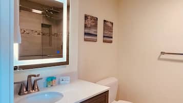 A bathroom with a large mirror, a sink, a toilet, and two framed pictures on the wall.