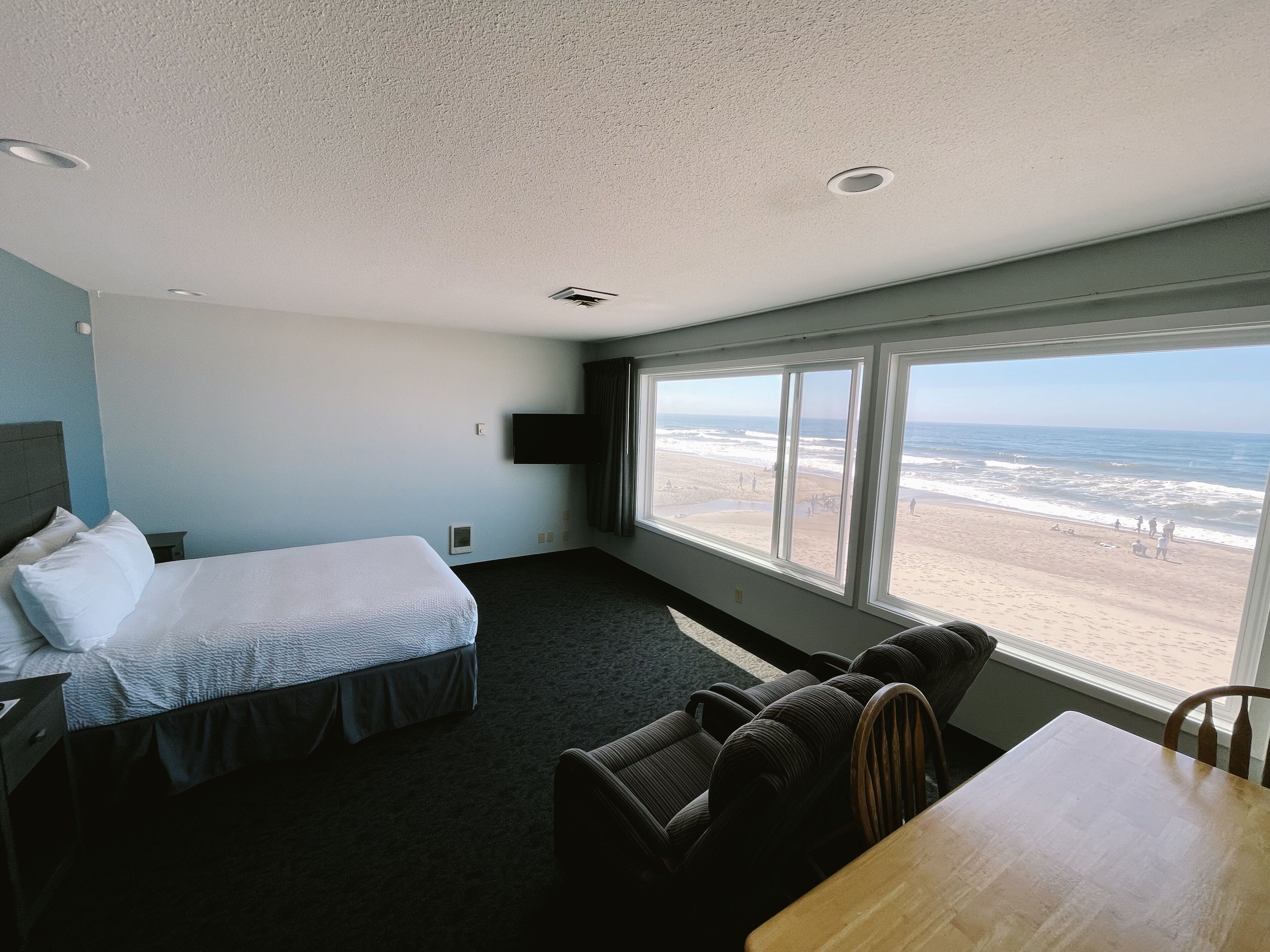 Een hotelkamer met een bed, een zithoek met een tafel en een groot raam met uitzicht op het strand.