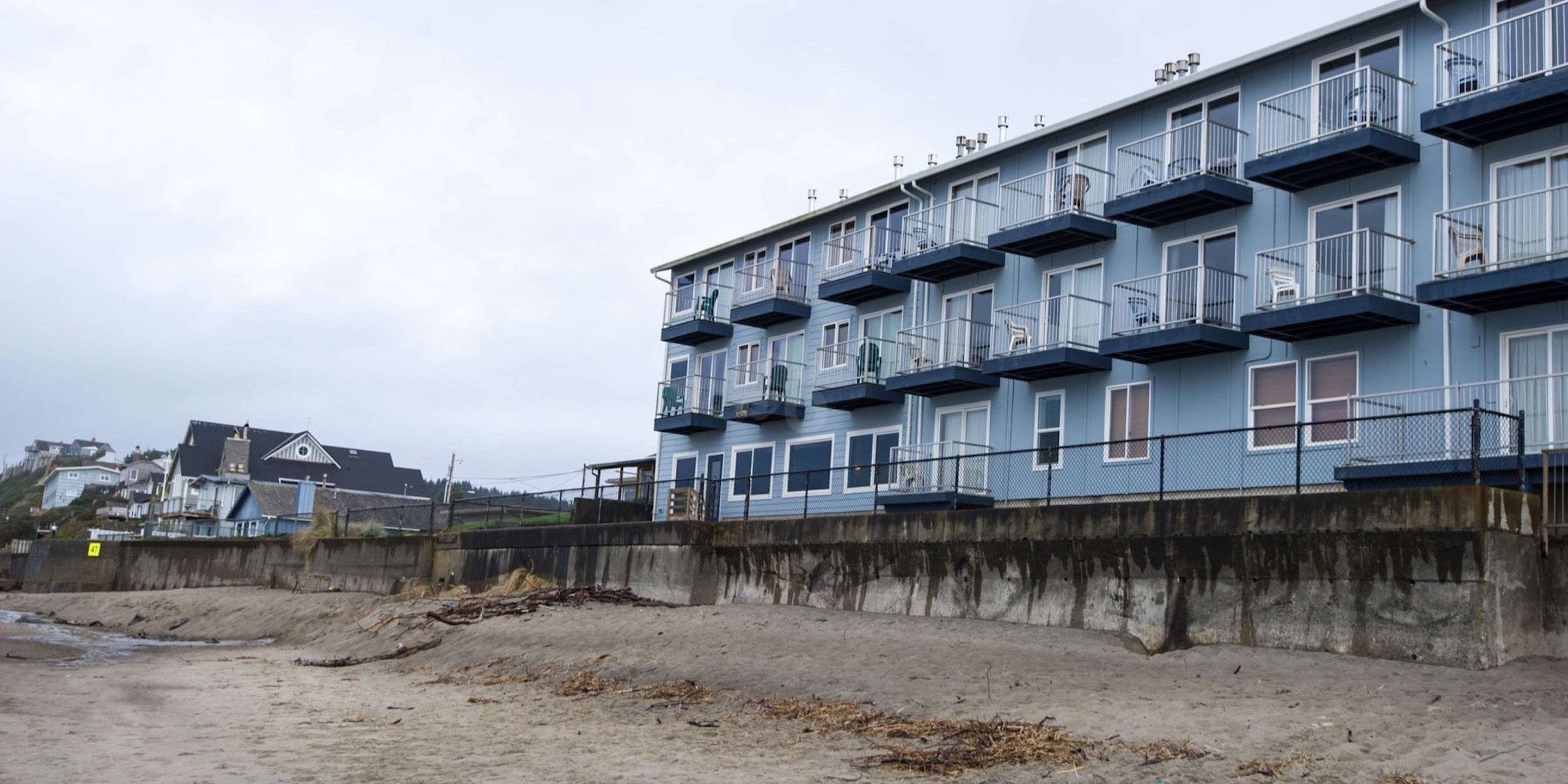 A multi-story building with balconies, a concrete retaining wall, and a sandy beach in the foreground.