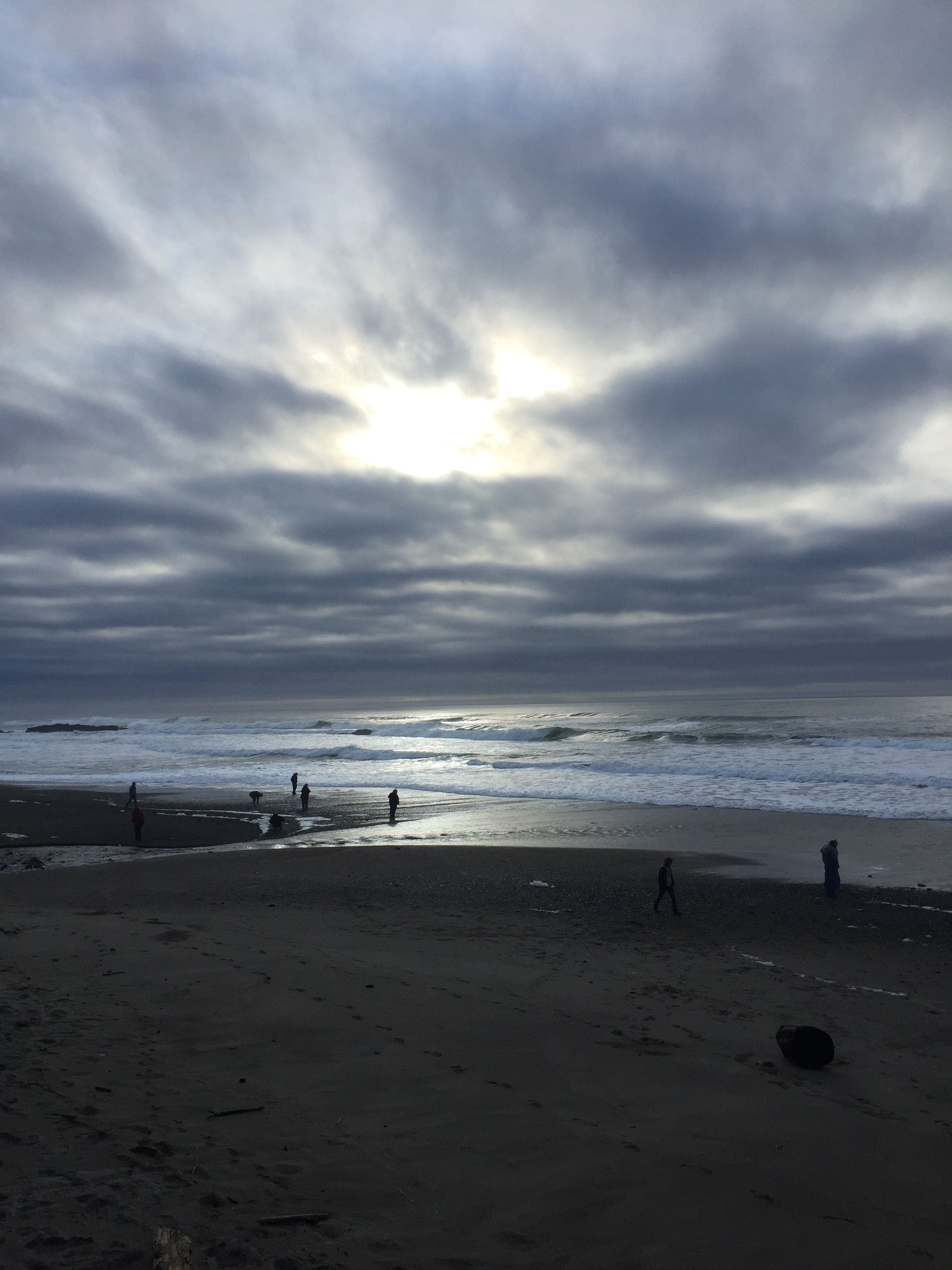Una playa con gente caminando por la orilla bajo un cielo nublado.