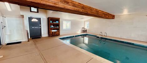 An indoor swimming pool with a wooden ceiling, a door, and a chair.