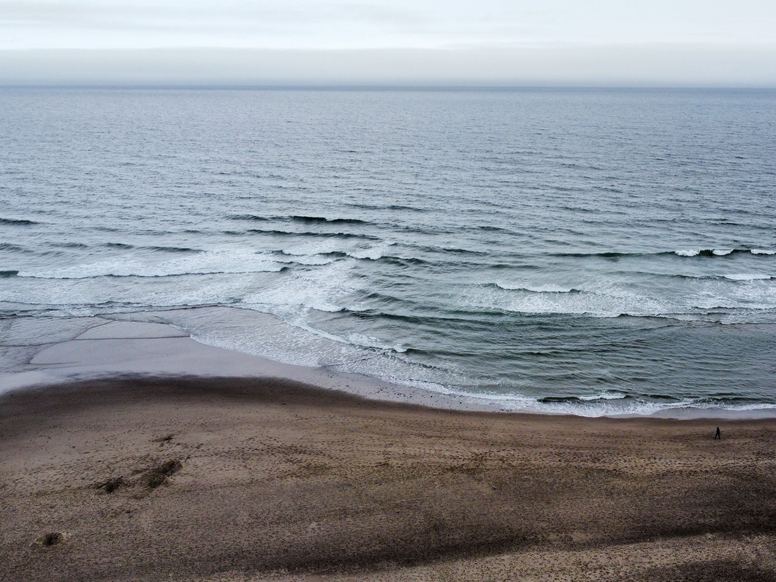 Ein Strand mit ankommenden Wellen, eine Person, die spazieren geht, und einem klaren Himmel.