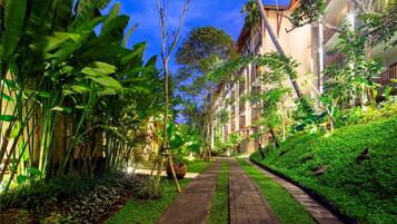 A pathway flanked by lush greenery and a building with multiple balconies.