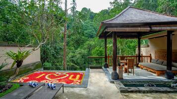 A covered outdoor seating area with a wooden table and chairs, a small pool, and a decorative tile design on the ground.
