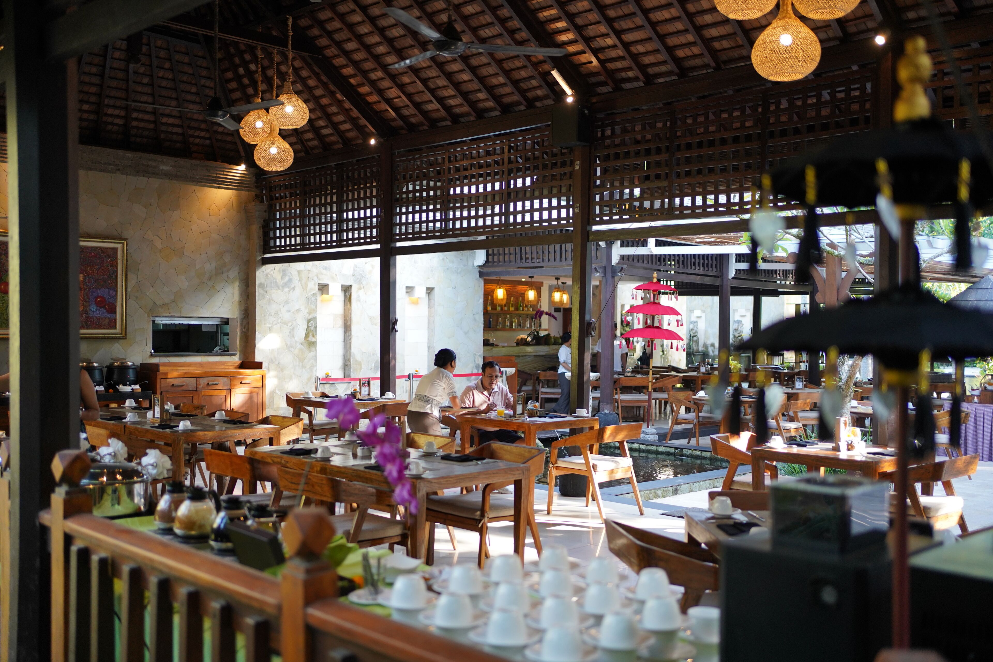 A restaurant with wooden furniture, hanging lights, and a stone wall.