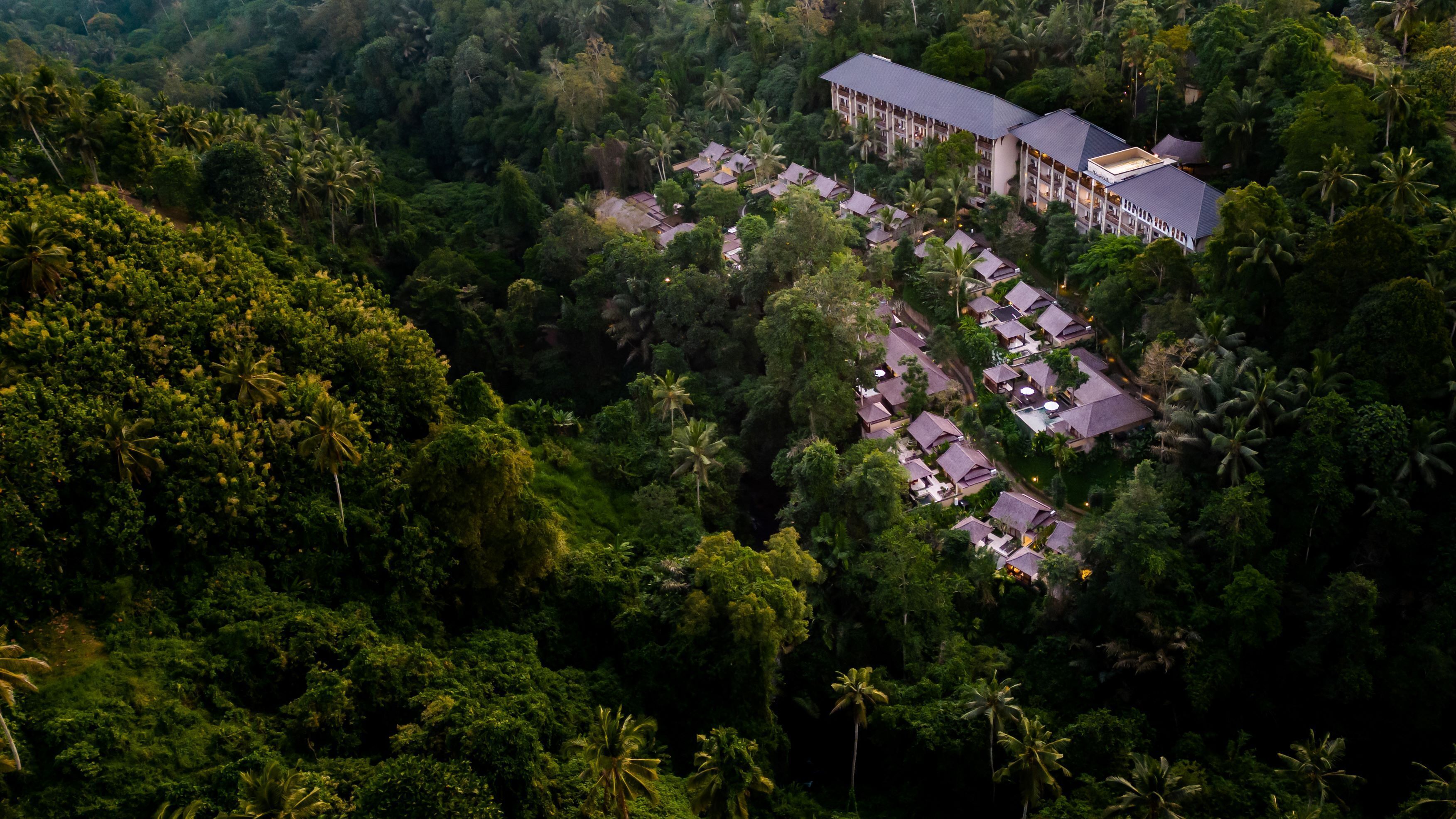 An aerial view of a resort with multiple bungalow-style buildings surrounded by dense tropical forest.