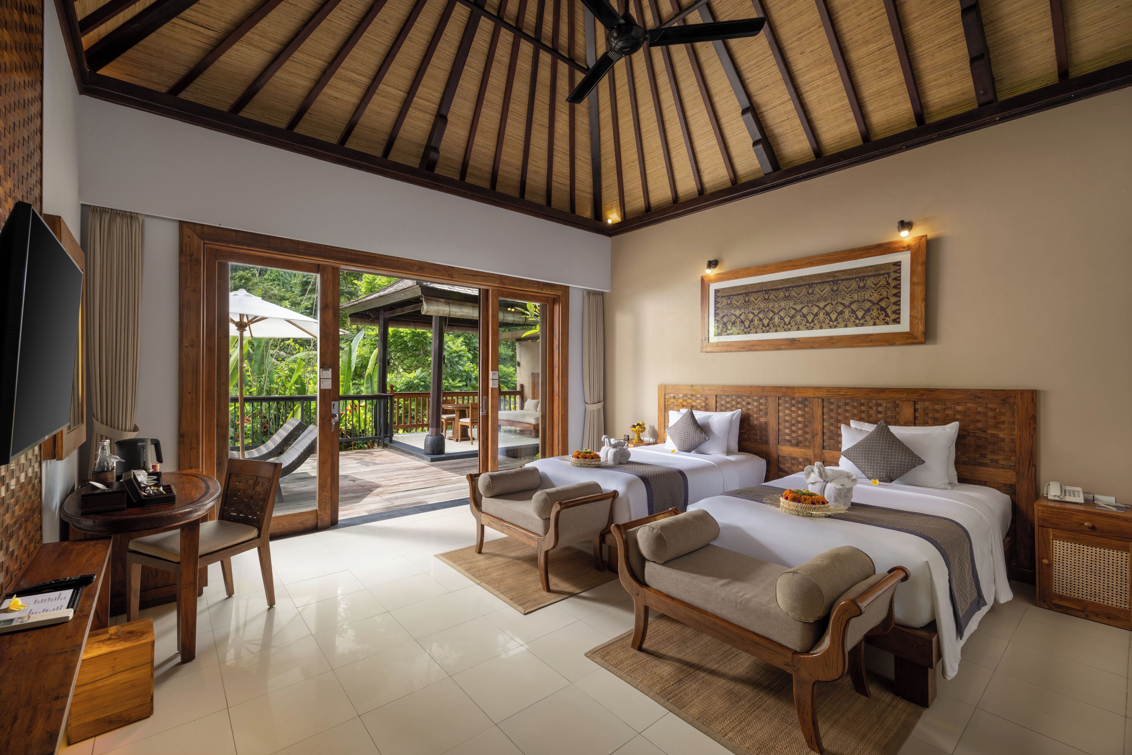 Quarto de hotel com uma cama grande, duas mesas de cabeceira, televisão e varanda com vista para áreas verdes.