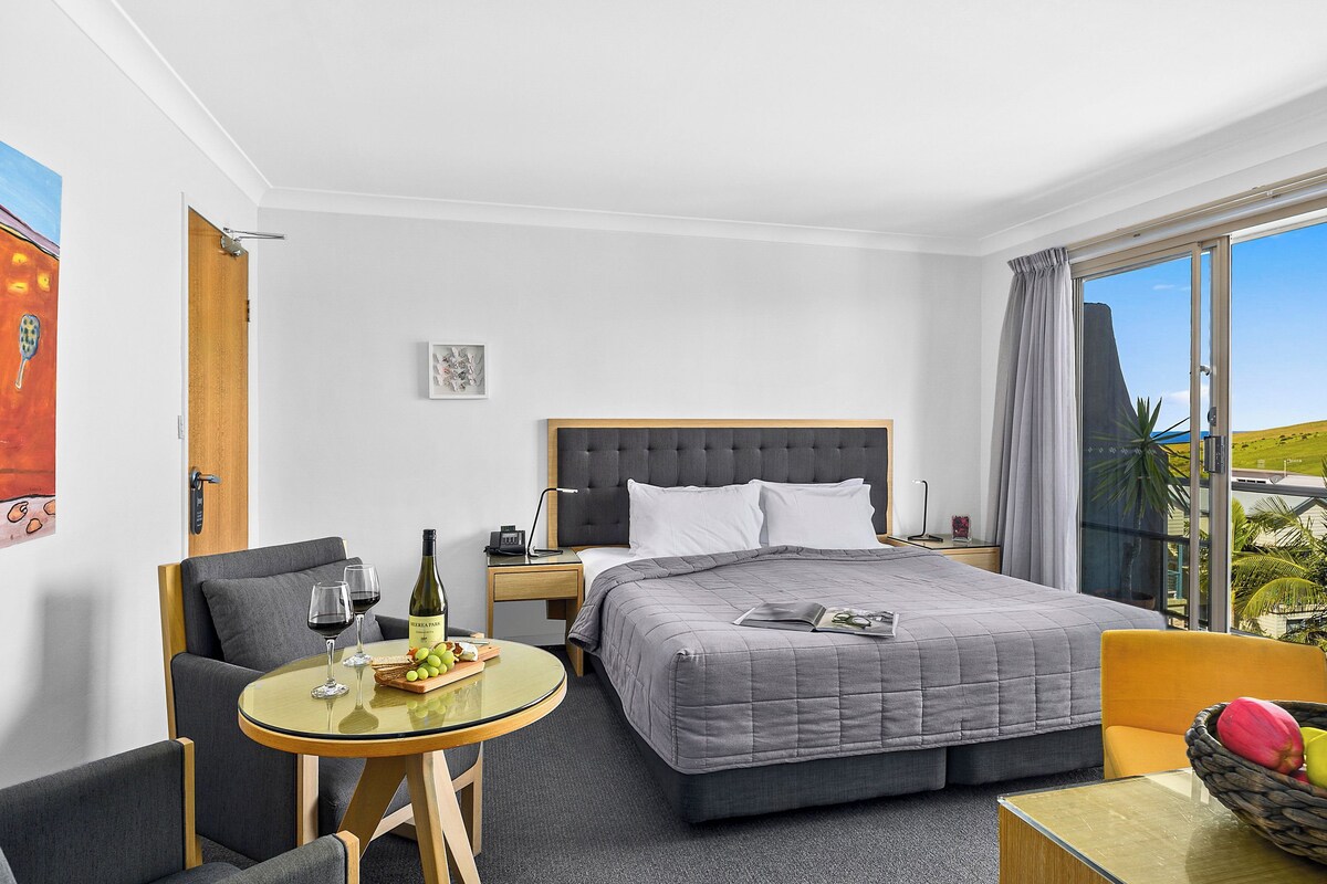 A hotel room with a bed, a round glass table, a sofa, and a view of the outdoors.
