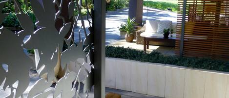 A modern outdoor seating area with a bench and a table, surrounded by a low hedge and a decorative metal fence.