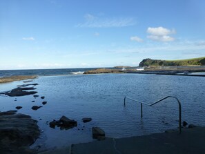 A coastal scene with a rocky shoreline, calm sea, and a clear sky. - Park Ridge Retreat (Gerringong)