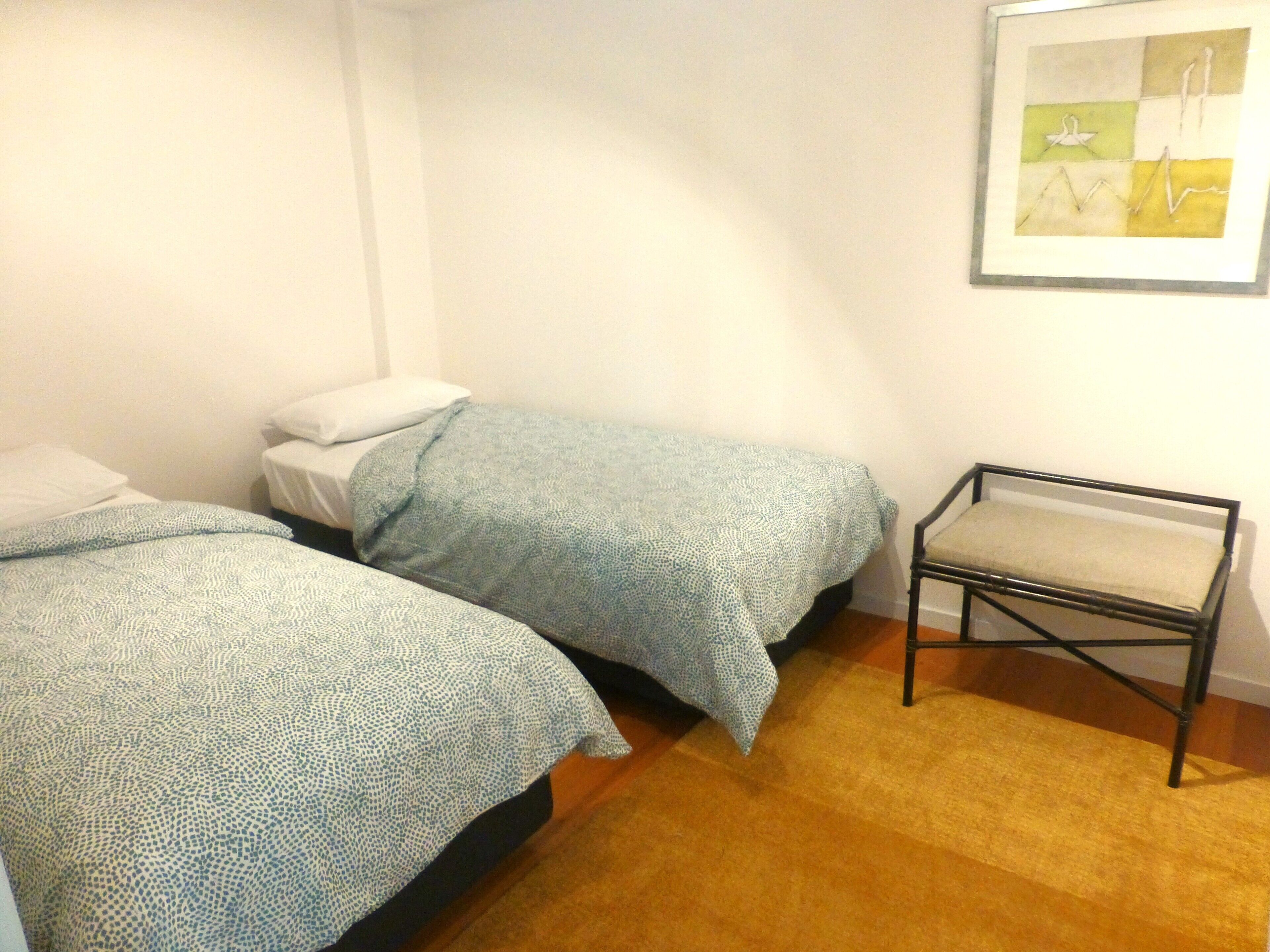 A bedroom with two single beds, a small table, and a framed abstract painting on the wall.