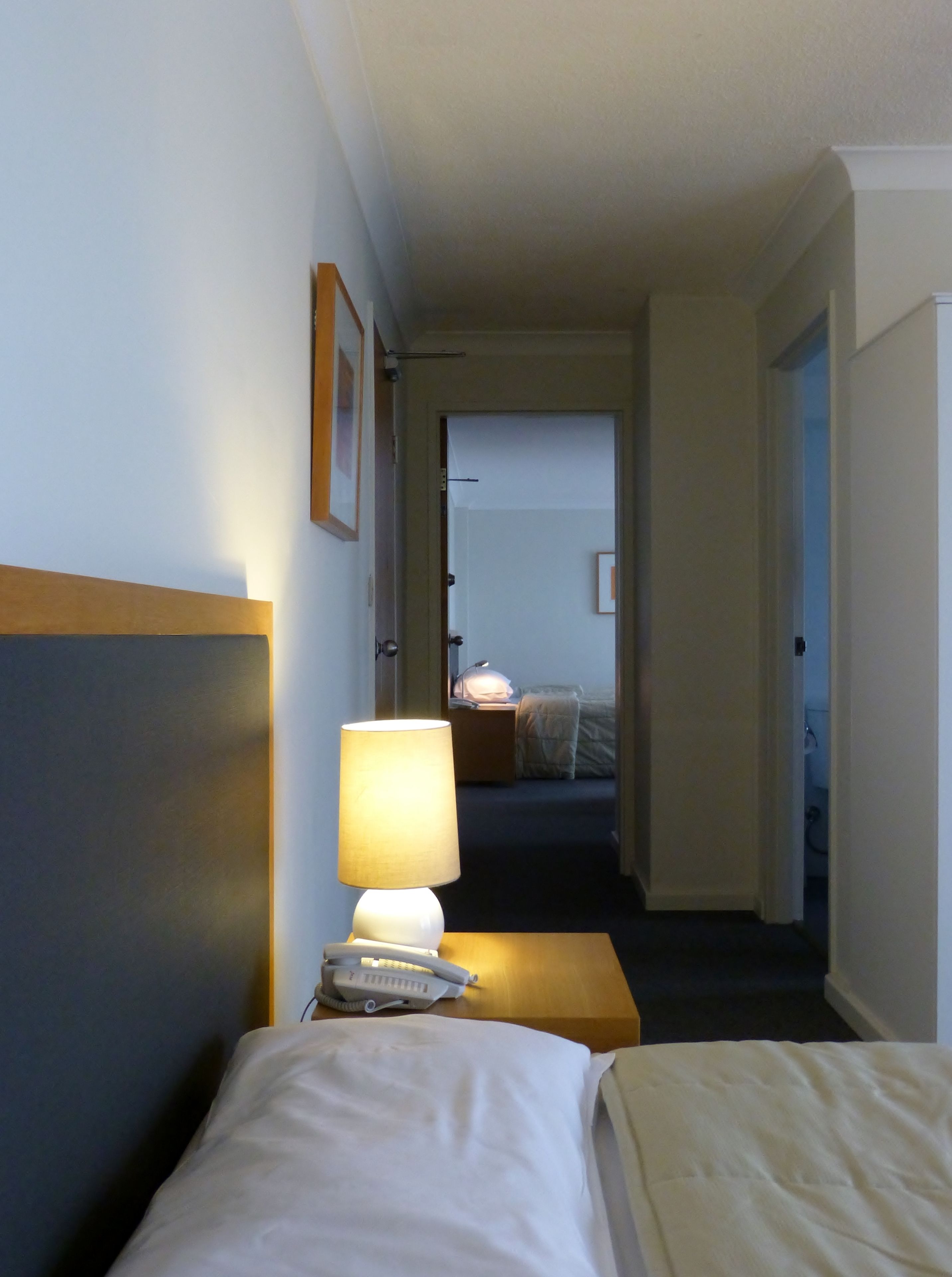A hotel room with a bed, bedside table, lamp, and a telephone.