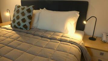 Una cama bien hecha con colcha acolchada, cabecera oscura y dos lámparas de noche.
