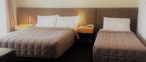 A hotel room with two beds, a nightstand with a lamp, and a small table.