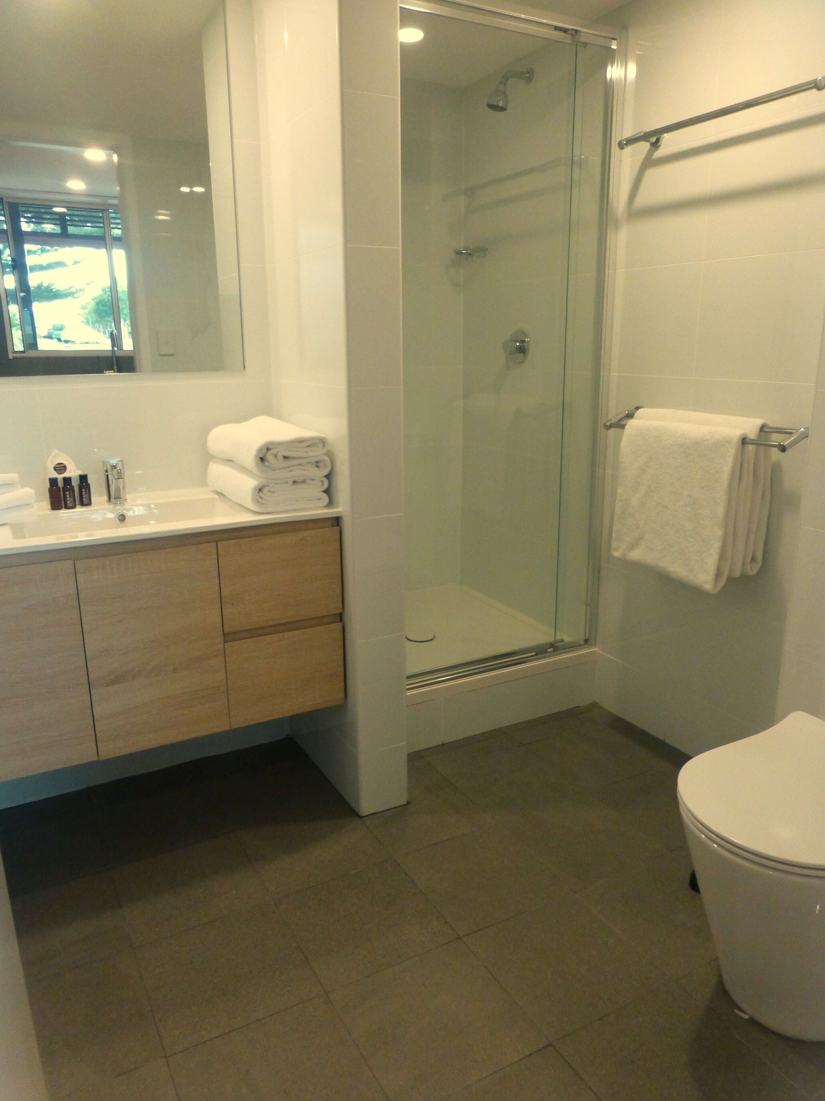 A modern bathroom with a glass-enclosed shower, a white sink with toiletries, and a toilet.
