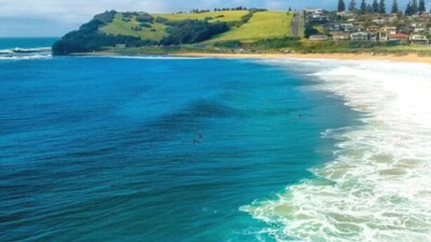 Un paisaje costero con playa, océano y una colina con edificios.