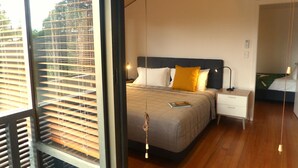 Un dormitorio moderno con una cama grande, una mesita de noche y vistas al exterior a través de una ventana con persianas.