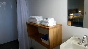Un bagno con uno scaffale in legno pieno di asciugamani piegati, un lavabo con uno specchio e un box doccia.