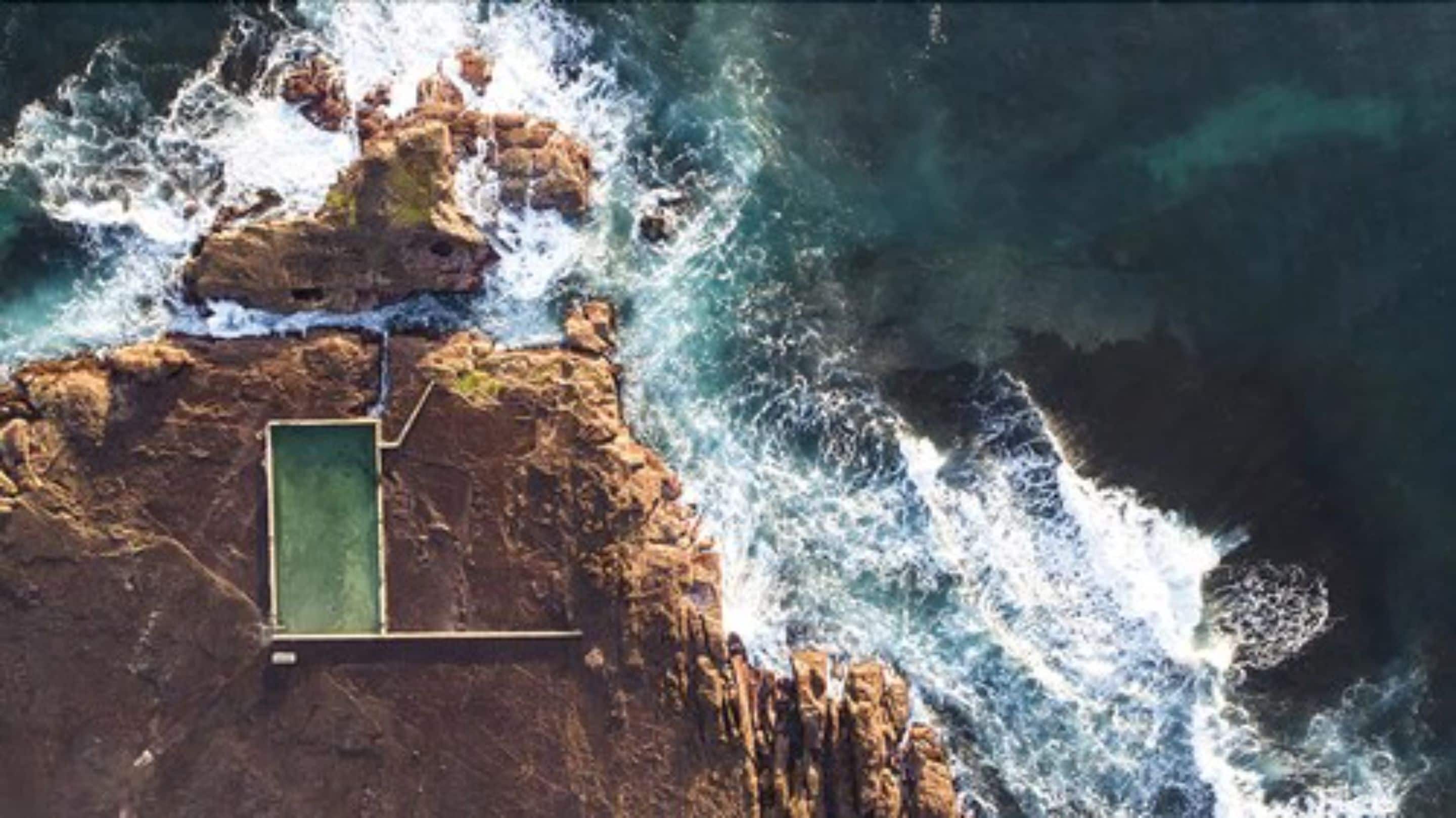 An aerial view of a rocky coastline with a swimming pool.