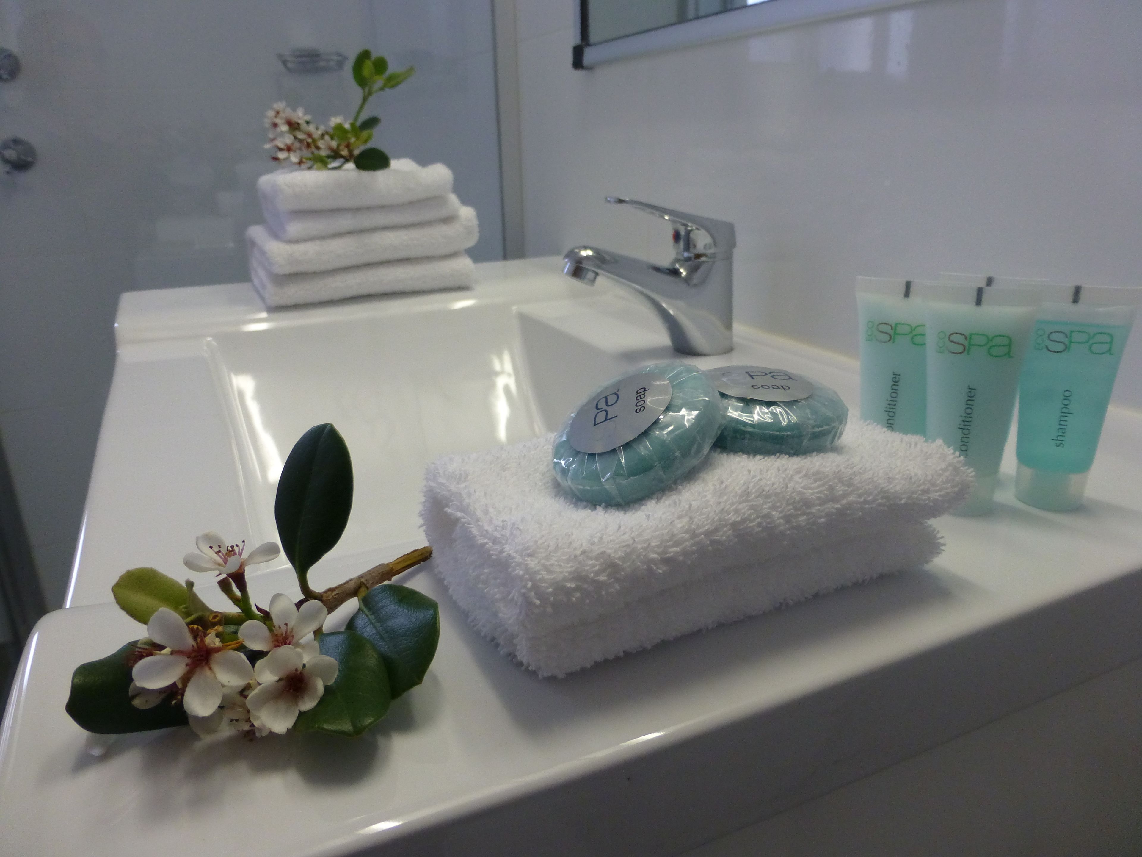 Ett badrum med en vit tvättställ, en hög med vita handdukar och tre tuber med produkter för spa-behandlingar.