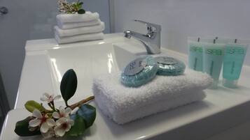 A bathroom with a white sink, a stack of white towels, and three spa product tubes.
