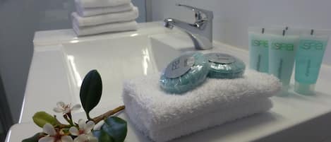 Ett badrum med en vit tvättställ, en hög med vita handdukar och tre tuber med produkter för spa-behandlingar.