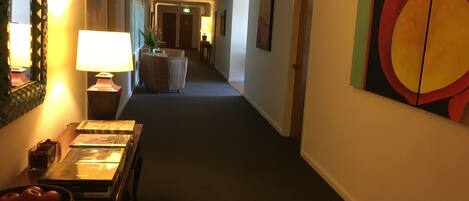 A hotel hallway with a reception desk, a large painting on the wall, and an exit sign.
