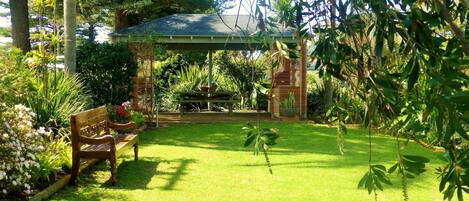 A garden with a gazebo, a wooden bench, and various plants.