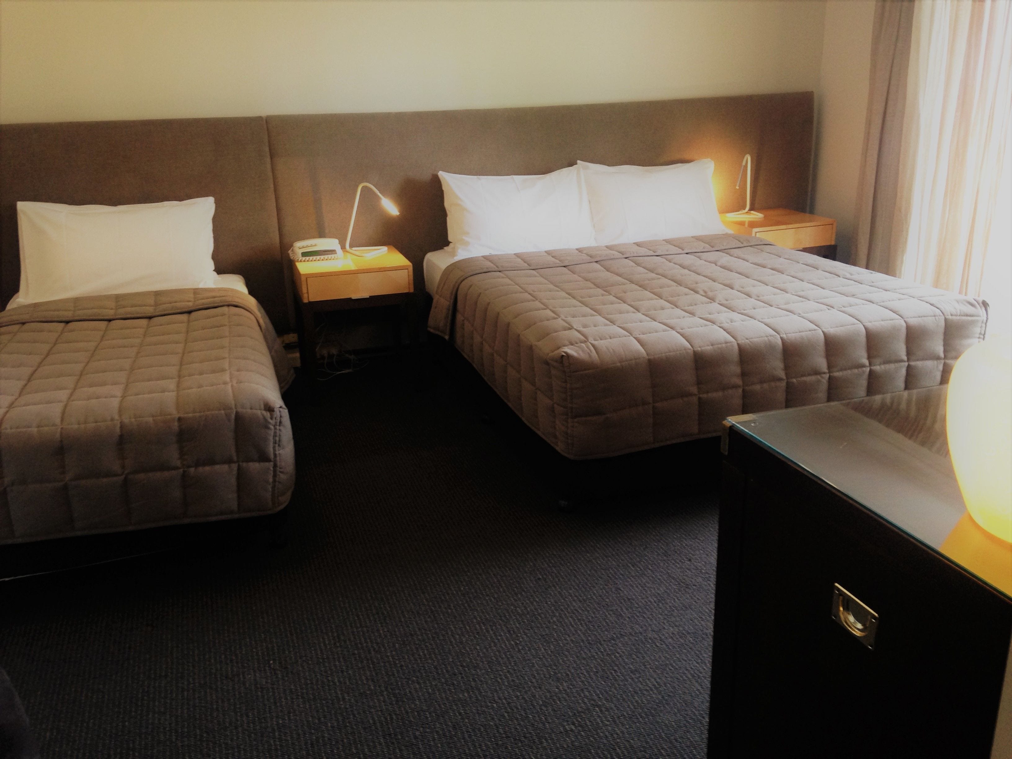 A hotel room with two beds, a nightstand with a lamp, and a dresser.