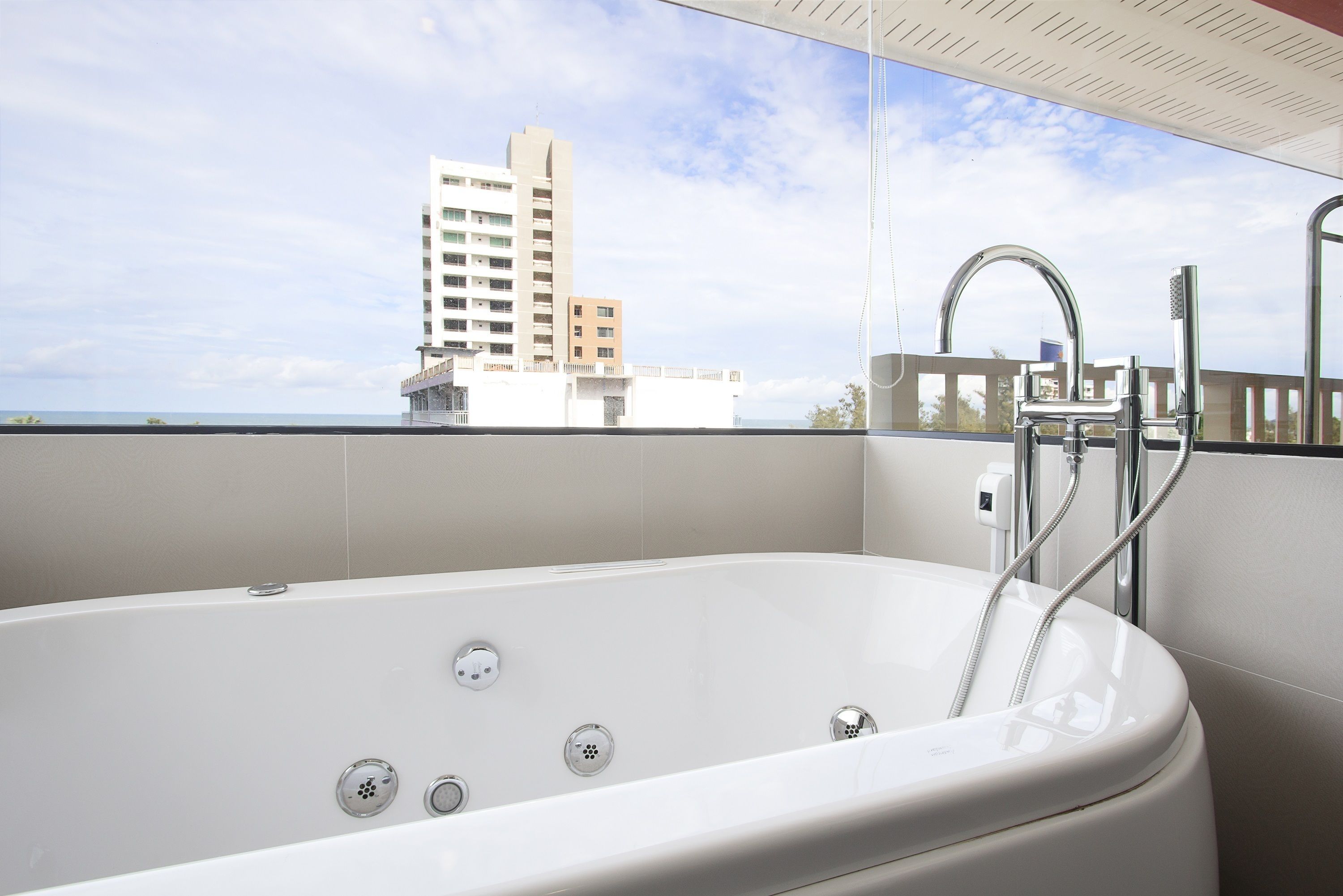 A modern bathroom with a large bathtub, a showerhead, and a view of a tall building through a glass partition.