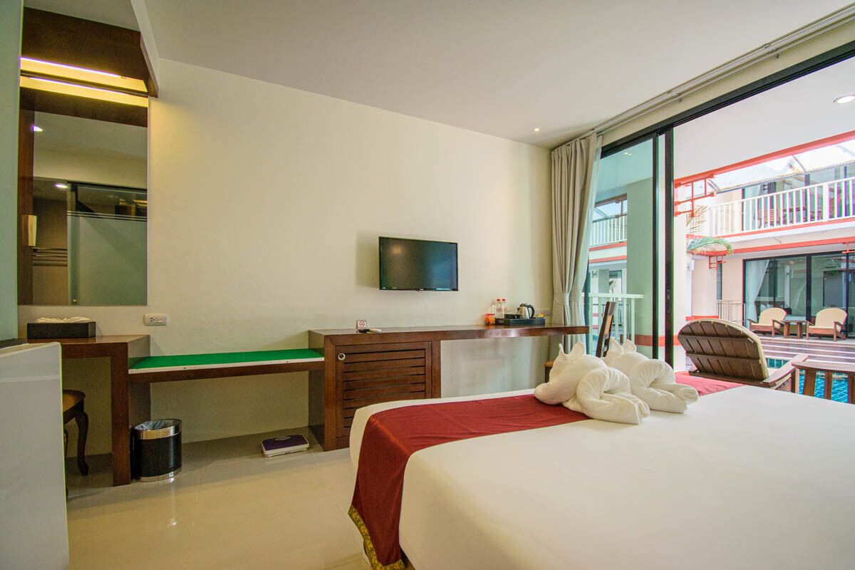 Een hotelkamer met een bed, een bureau, een televisie en een balkon met zitplaatsen.