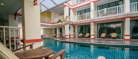 An indoor swimming pool with multiple levels, seating areas, and a glass ceiling.