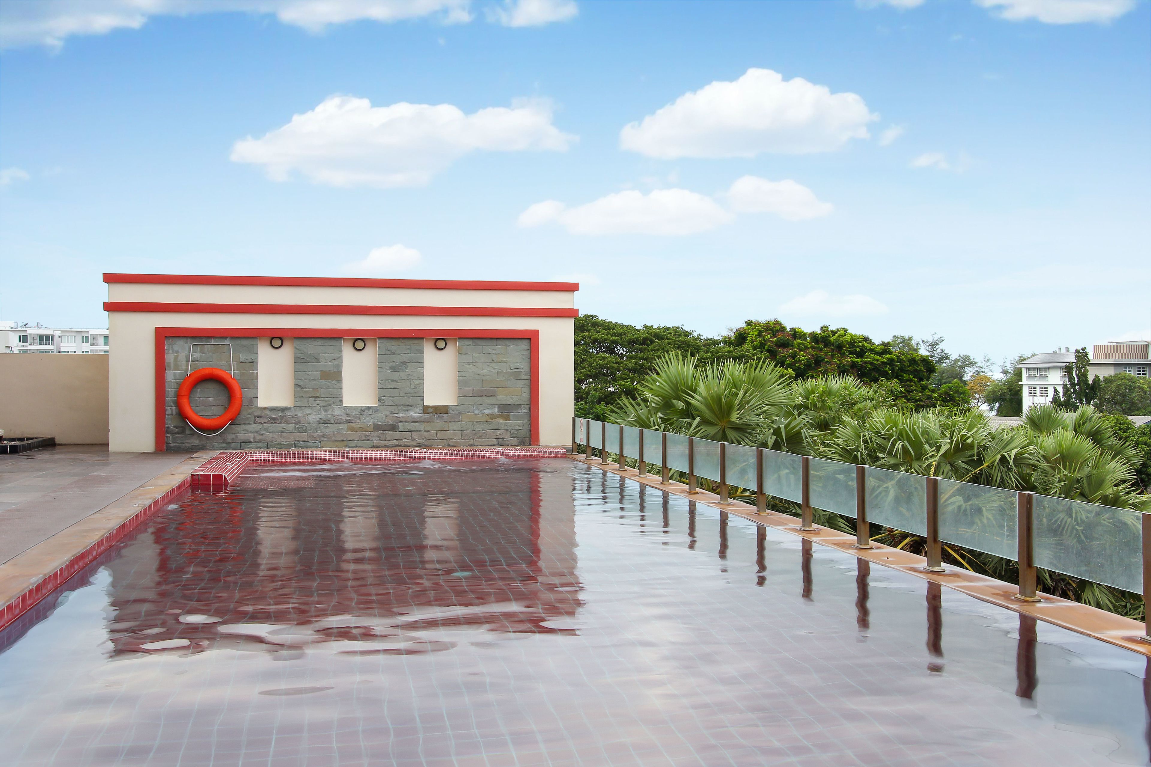 A rooftop swimming pool with a red and white building, a lifebuoy, and a glass railing.