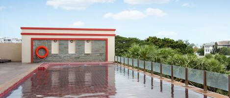 A rooftop swimming pool with a red and white building, a lifebuoy, and a glass railing.