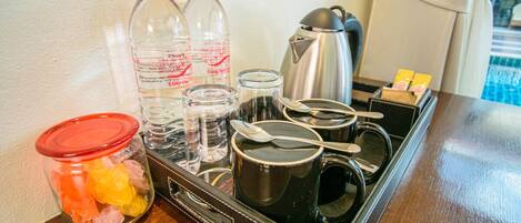A kitchen area with a coffee maker, two bottles of water, a jar of snacks, and a kettle.
