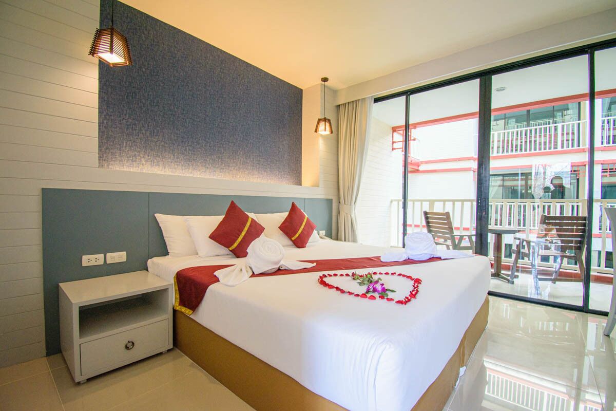 Une chambre d’hôtel avec un grand lit, une table de chevet, une vue sur le balcon extérieur et un mur orné d’un motif texturé.