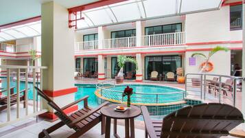 A multi-level indoor swimming pool with lounge chairs and tables, surrounded by balconies and a restaurant.