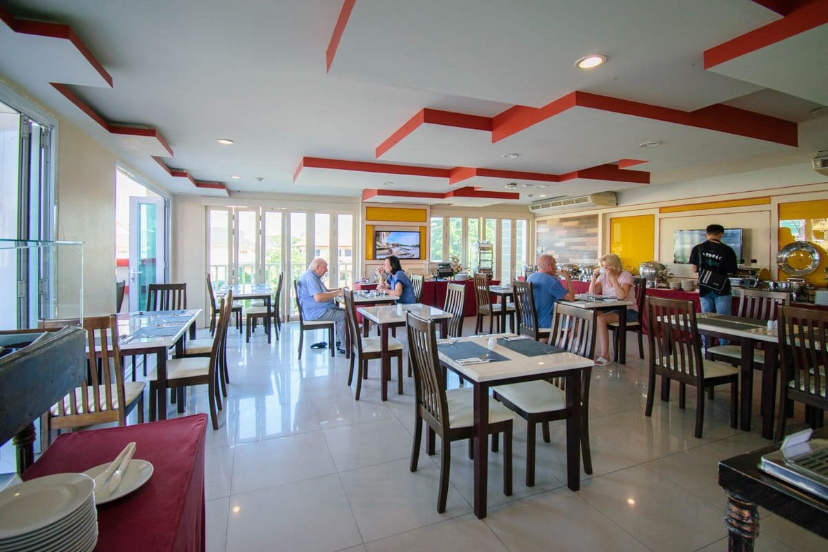 Un restaurante espacioso con numerosas mesas y sillas, ventanas amplias y un diseño de techo moderno.