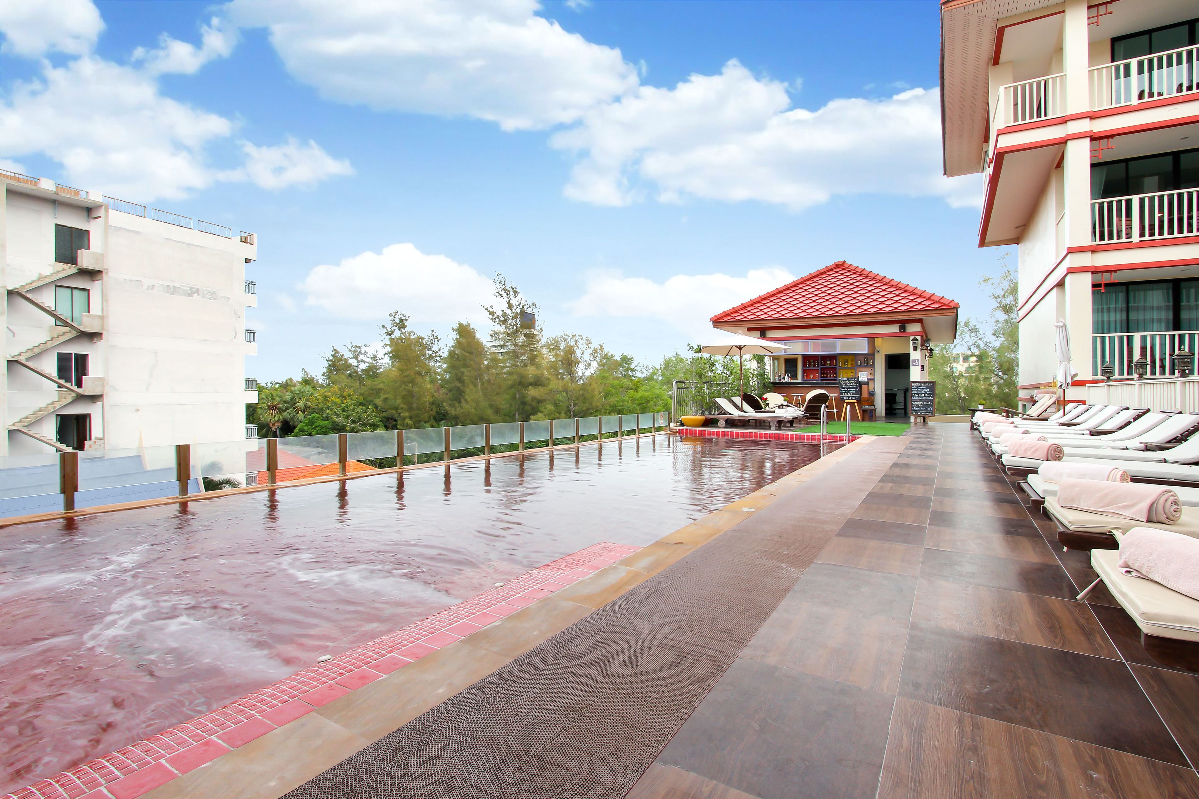 Un área de piscina en la azotea con sillones de descanso y un edificio con techo rojo al fondo.