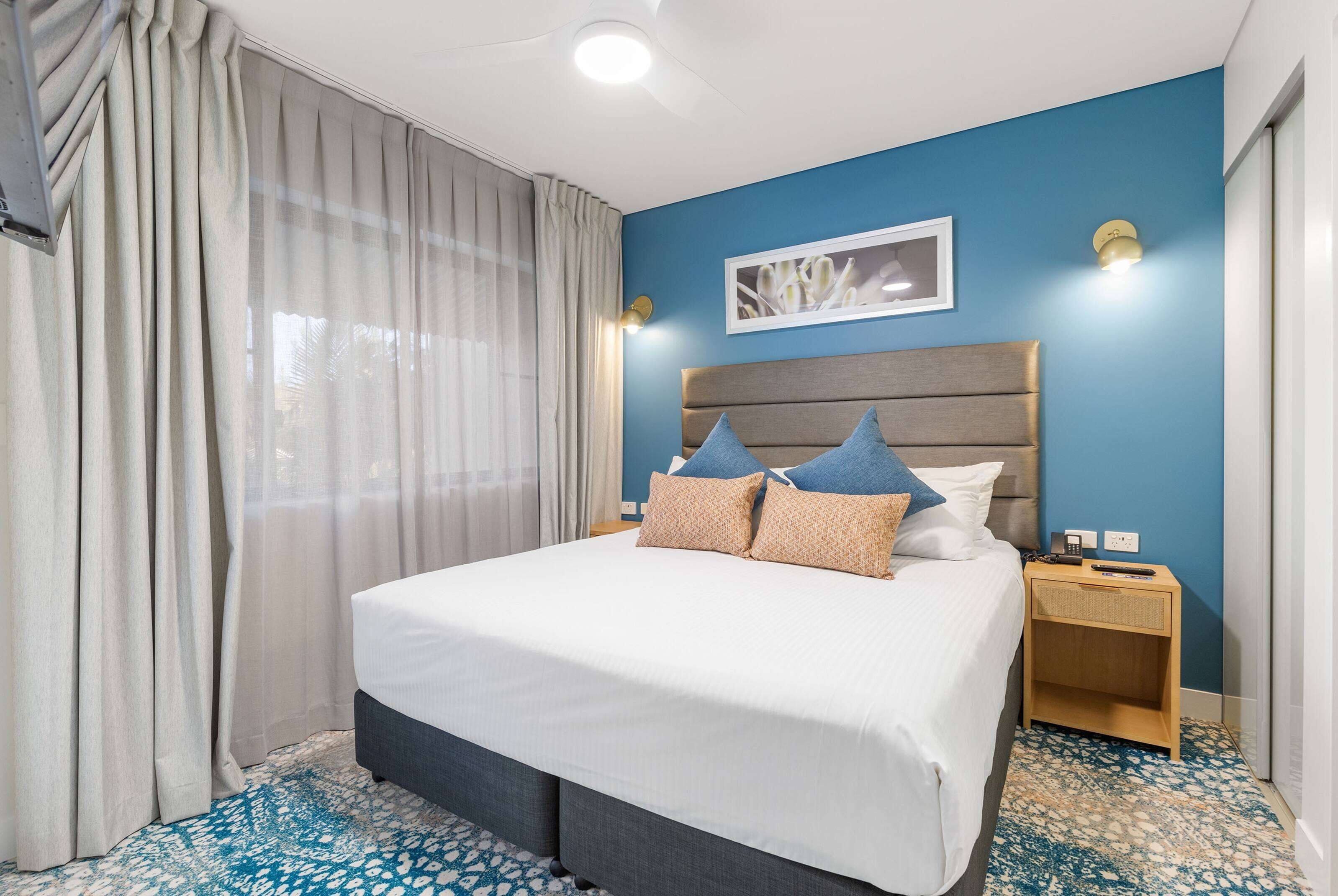 A hotel room with a large bed, a nightstand, and a blue wall.