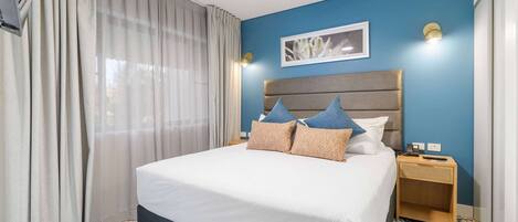 Una habitación de hotel con una cama grande, una mesita de noche y una pared azul.