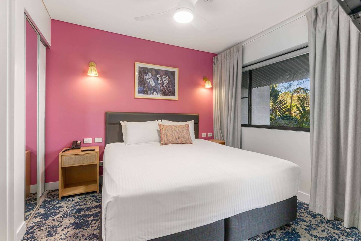 A hotel room with a large bed, two bedside lamps, a nightstand, a window with curtains, and a framed picture on the wall.