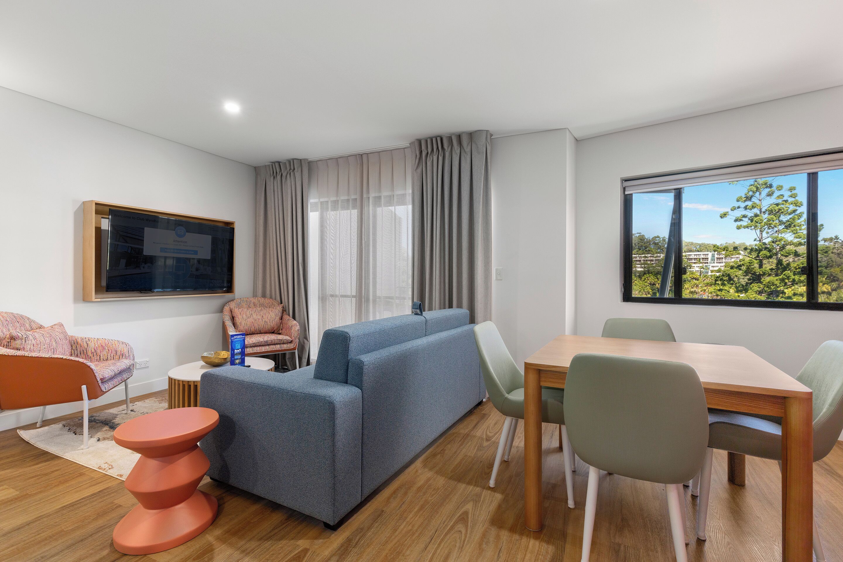 A modern living room with a sofa, chairs, a dining table, and a TV.
